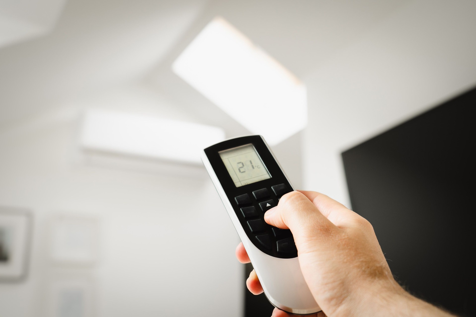 Aircon remote control Aircon remote control set to 21°C, pointed at a wall-mounted air-to-air heat pump in a bright living room.